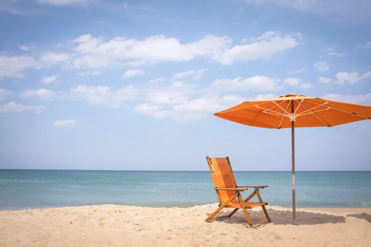 A tranquil beach scene with a single beach chair and umbrella set in the sand, facing the calm ocean. The scene is serene and evokes relaxation, with the open water stretching into the distance. It embodies the peaceful, ever-changing seascape referenced in the section.