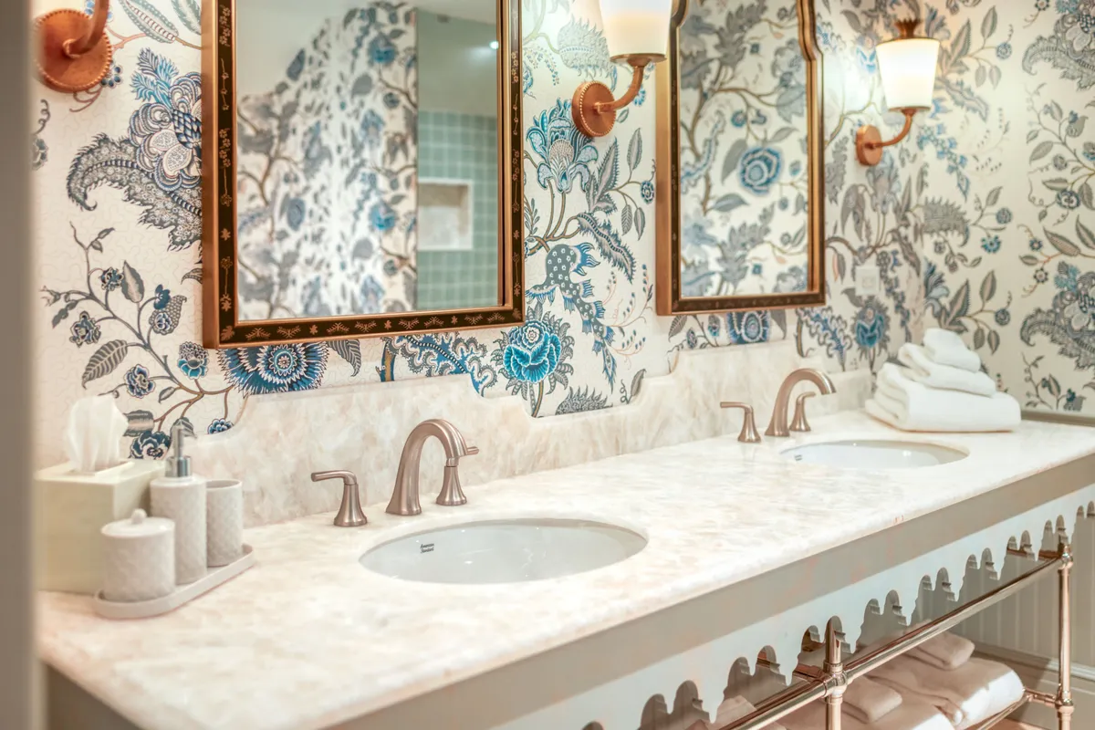 A sophisticated bathroom interior featuring double sinks with ornate mirrors, floral wallpaper, and stacks of plush, luxurious towels. The setting exudes a calming atmosphere, ideal for self-care routines and relaxation.