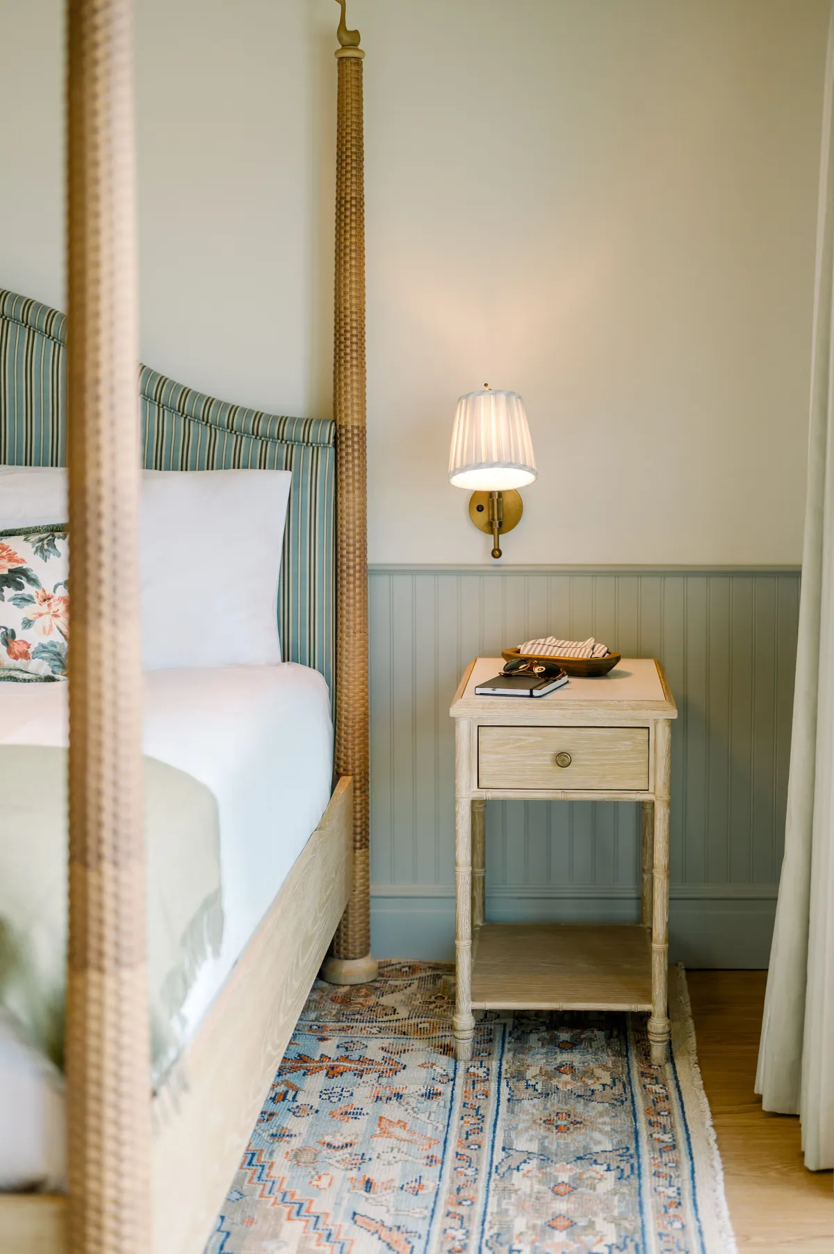 A serene bedroom corner with a canopy bed, nightstand, wall lamp, and soft rug, creating a peaceful ambiance perfect for unwinding, reading, or quiet conversations.