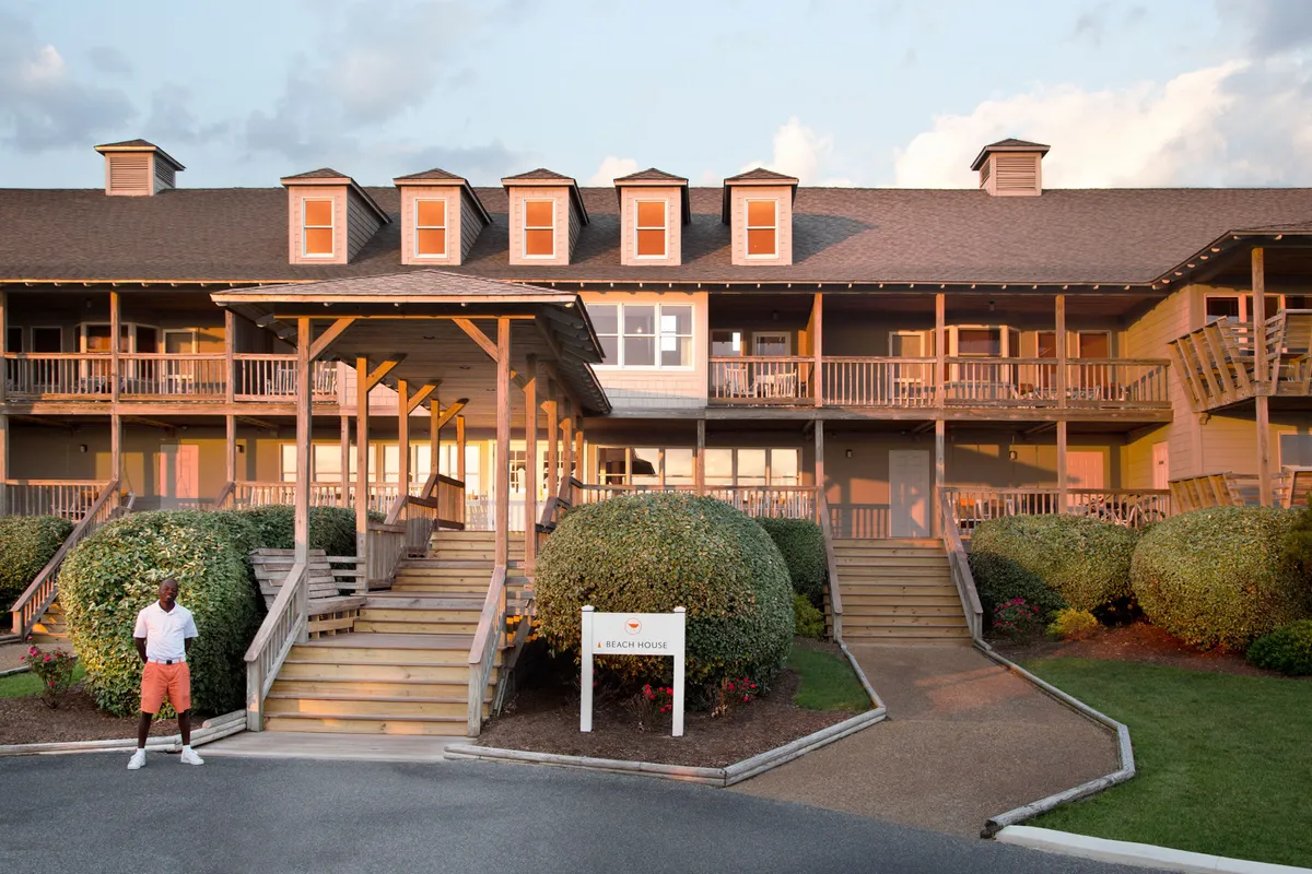 The main entrance to the resort’s beach house, featuring welcoming steps, neatly trimmed hedges, and a visible sign. The cheerful exterior suggests easy beach access and an inviting atmosphere for social gatherings and exploration.