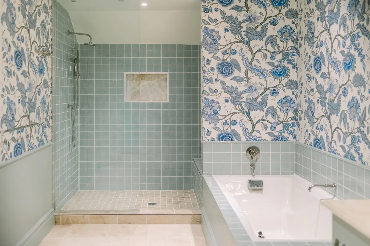A serene bathroom scene highlighting a spacious bathtub, decorative floral wallpaper, and a modern shower area. Soft lighting enhances the calming, spa-like ambiance, inviting guests to unwind and rejuvenate.